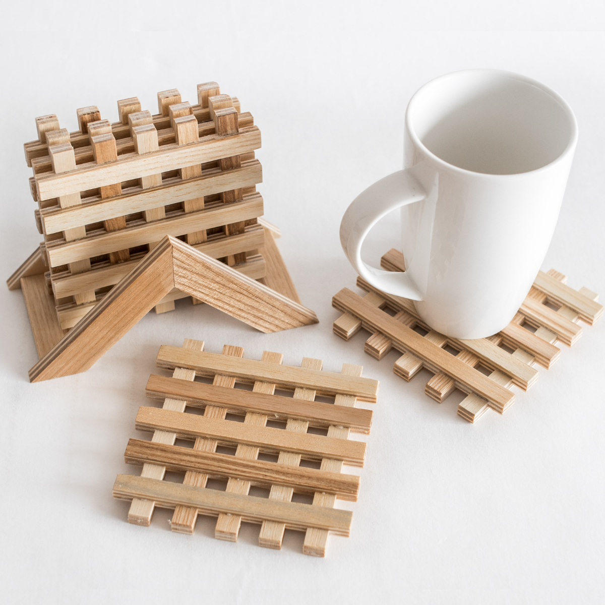 Handmade wooden coasters in a lattice pattern displayed with a white mug on one. Showcasing their natural wood tones and craftsmanship.
